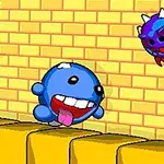 A colorful cartoon-style character, a blue rounded creature with a big grin and outstretched tongue, is leaping over spikes and a spiked ball, while a small menacing purple creature hovers nearby against a brick wall background