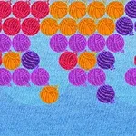 A colorful bubble shooter game display featuring various yarn-themed balls in red, orange, purple, and pink arranged in rows against a blue background