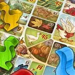 A colorful board game layout featuring various tiles with illustrations of nature, animals, and numbered spaces, along with brightly colored player pieces in yellow, green, red, and blue