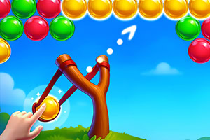 A colorful slingshot aiming at a formation of multi-colored balls against a bright blue sky, with a hand pulling back the slingshot and an arrow indicating the direction of the shot