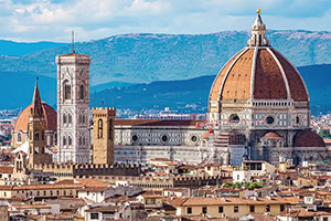 Florence skyline with the Florence Cathedral’s red-tiled dome and bell tower rising above historic buildings, with distant mountains under a blue sky