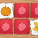 A colorful memory card game layout featuring a pumpkin, strawberries, and corn on red background cards, arranged in a grid on a wooden surface