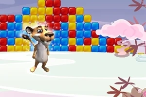 A cartoon animal character stands on an icy surface, waving cheerfully in front of a colorful wall made of stacked blue, red, and yellow blocks, with whimsical clouds and trees in the background