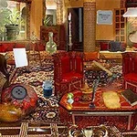 A cozy, intricate sitting room featuring ornate furniture, colorful textiles, a patterned rug, decorative accessories, and plants, creating a warm and inviting atmosphere